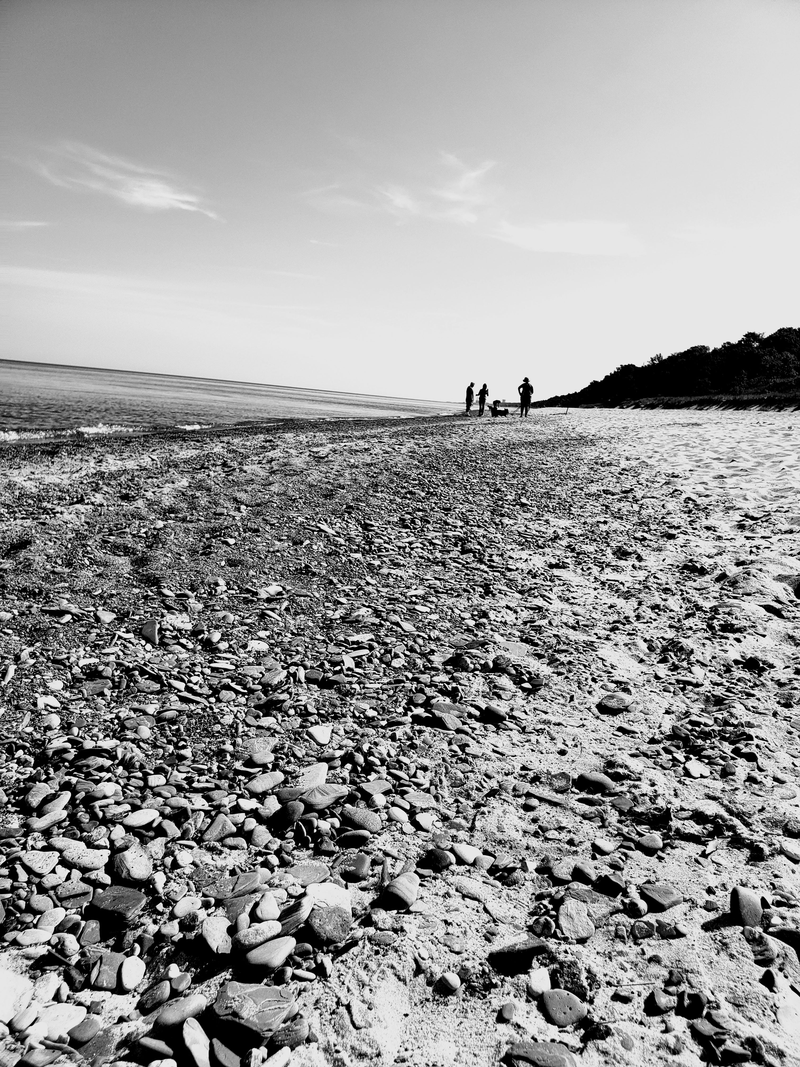 Black and white photo of a pebbly beach with people in the distance.