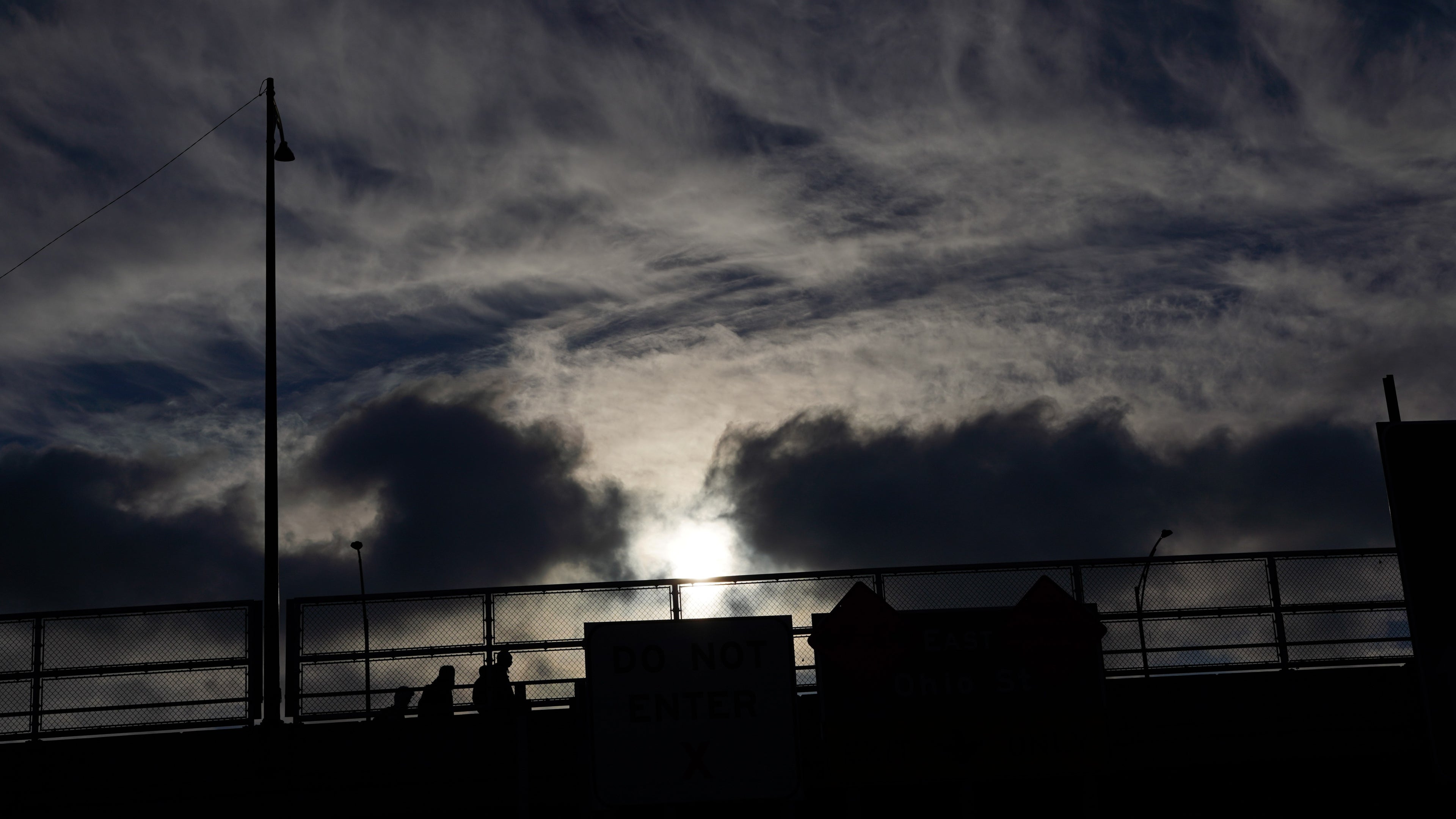 Dark silhouette of a bridge with people against a cloudy sky