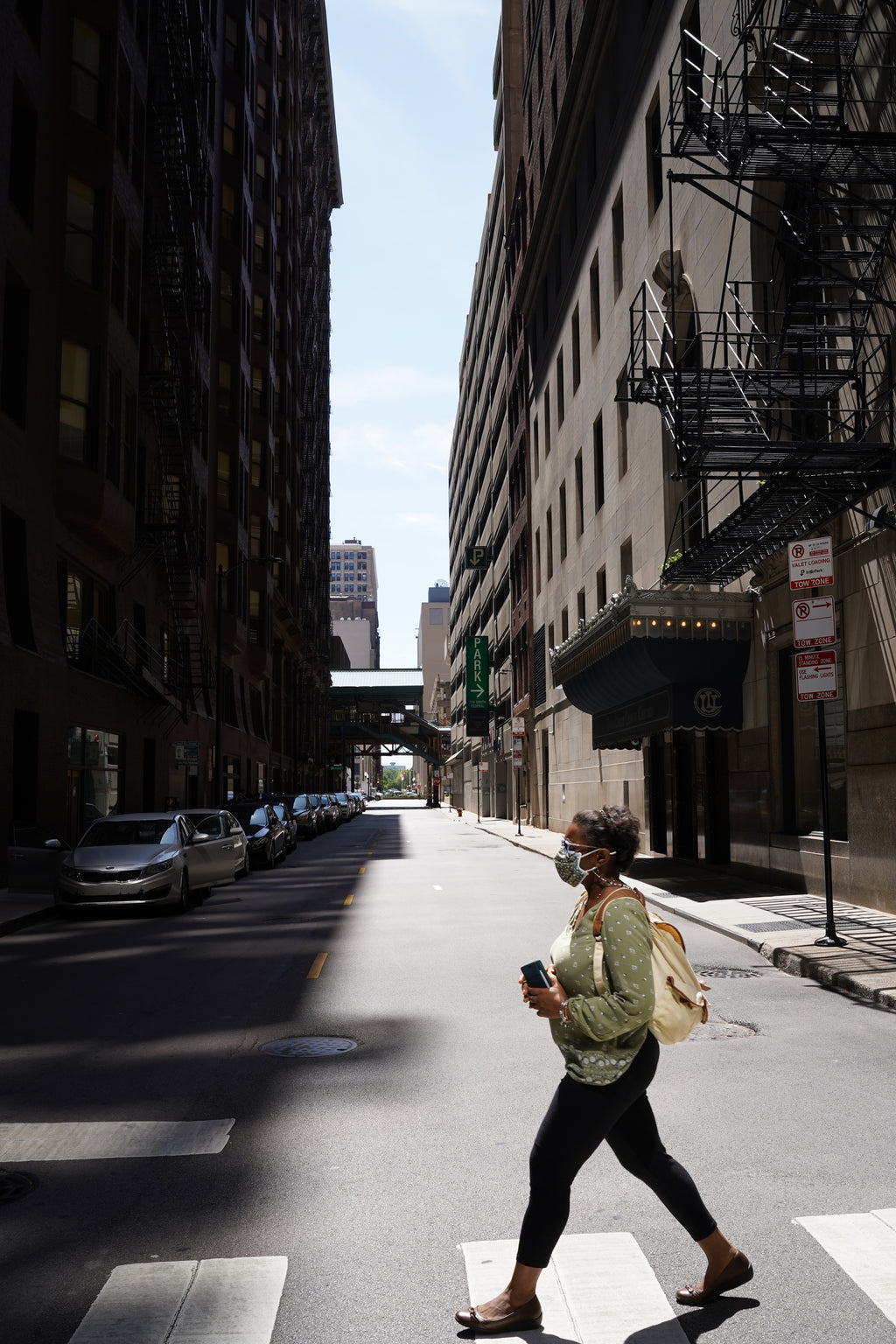Person walking on a city street with buildings and a clear sky.